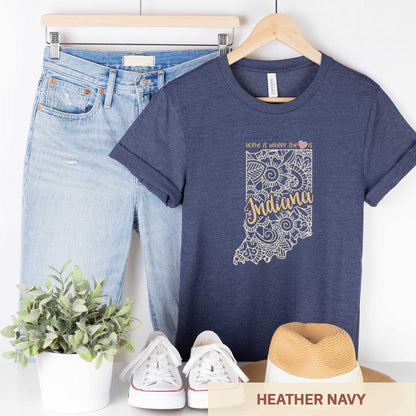 A hanging heather navy Bella Canvas t-shirt featuring a mandala in the shape of Indiana with the words home is where the heart is.
