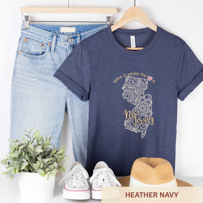 A hanging heather navy Bella Canvas t-shirt featuring a mandala in the shape of New Jersey with the words home is where the heart is.