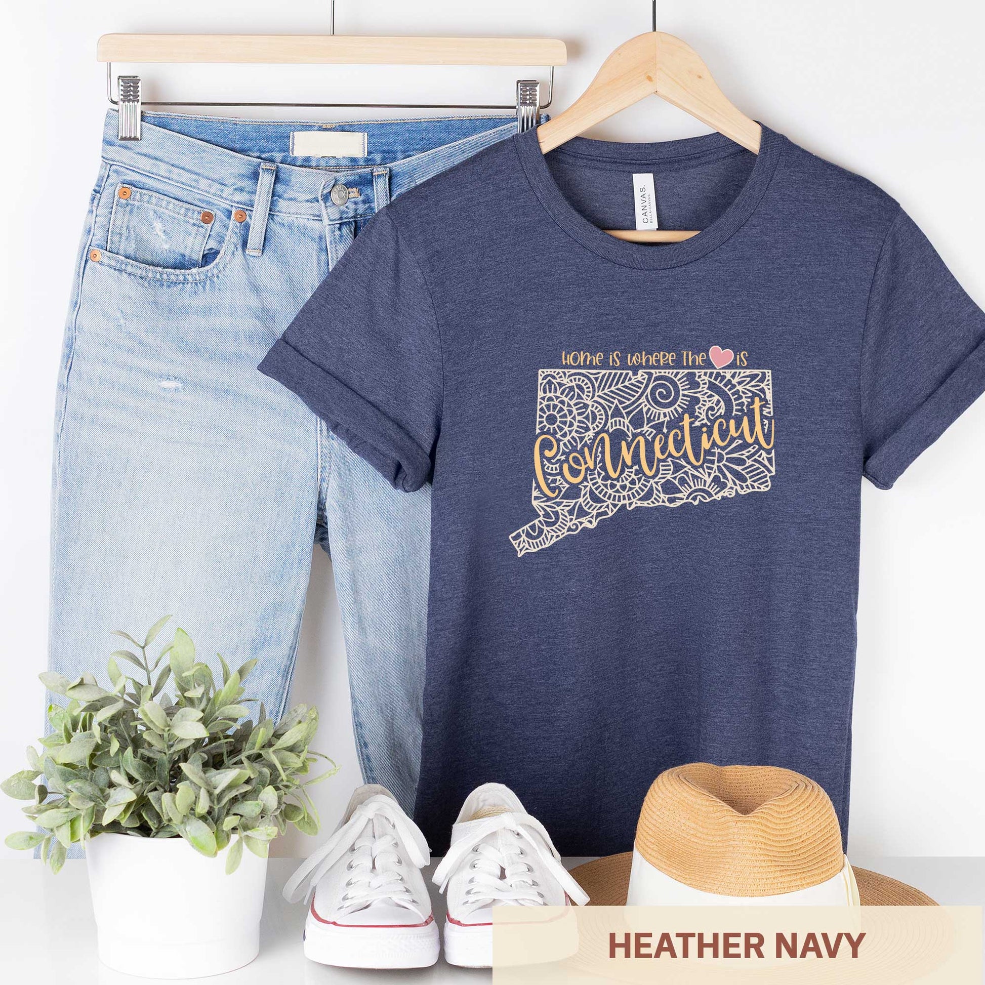 A hanging heather navy Bella Canvas t-shirt featuring a mandala in the shape of Connecticut with the words home is where the heart is.