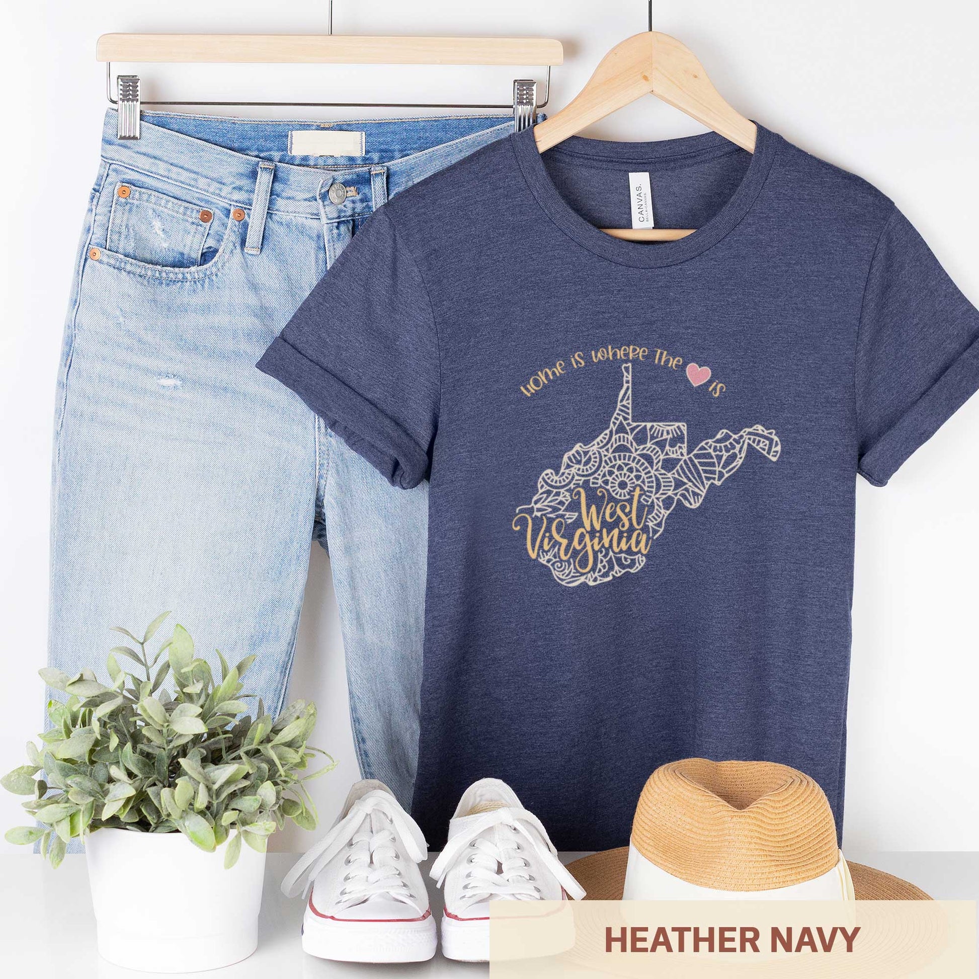 A hanging heather navy Bella Canvas t-shirt featuring a mandala in the shape of West Virginia with the words home is where the heart is.