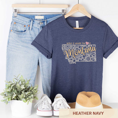 A hanging heather navy Bella Canvas t-shirt featuring a mandala in the shape of Montana with the words home is where the heart is.