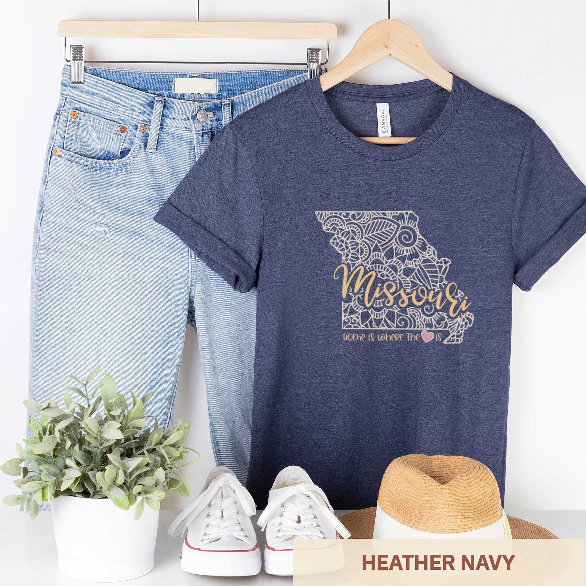 A hanging heather navy Bella Canvas t-shirt featuring a mandala in the shape of Missouri with the words home is where the heart is.