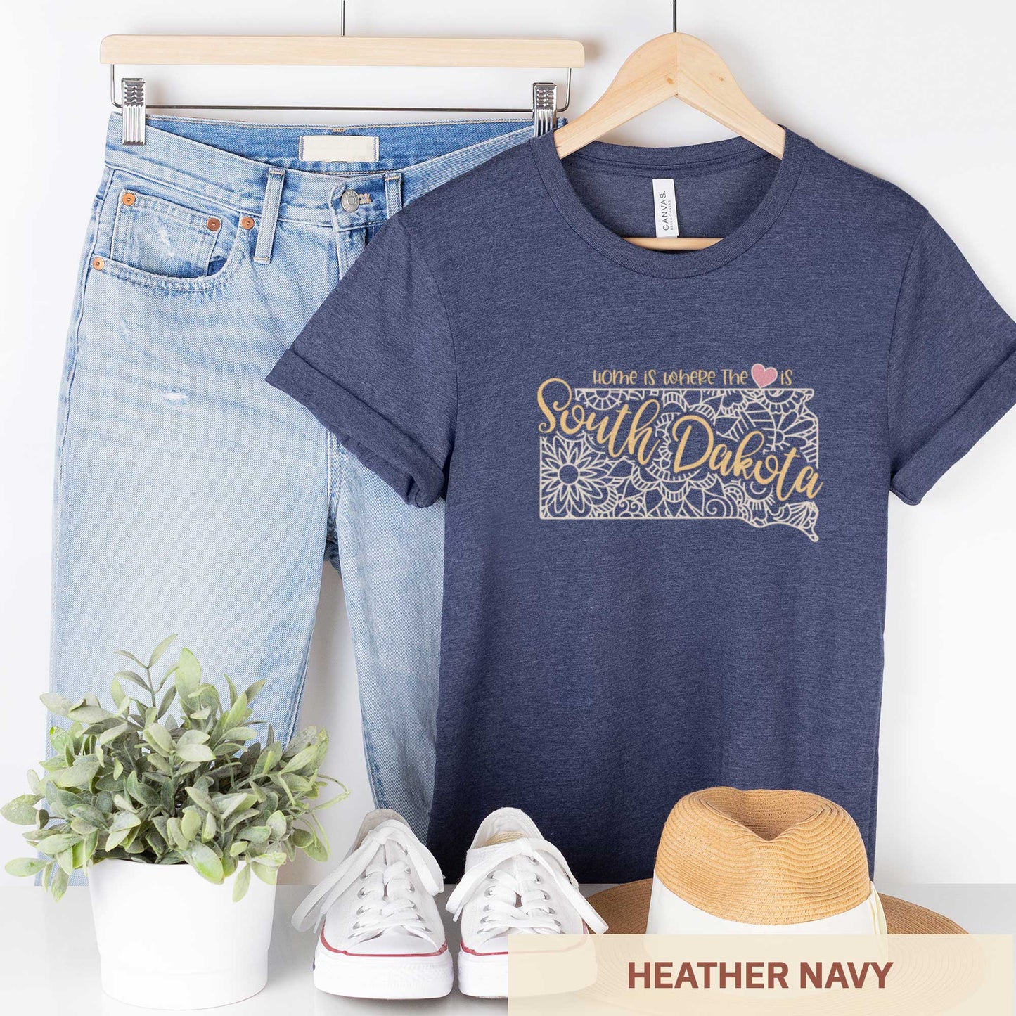 A hanging heather navy Bella Canvas t-shirt featuring a mandala in the shape of South Dakota with the words home is where the heart is.