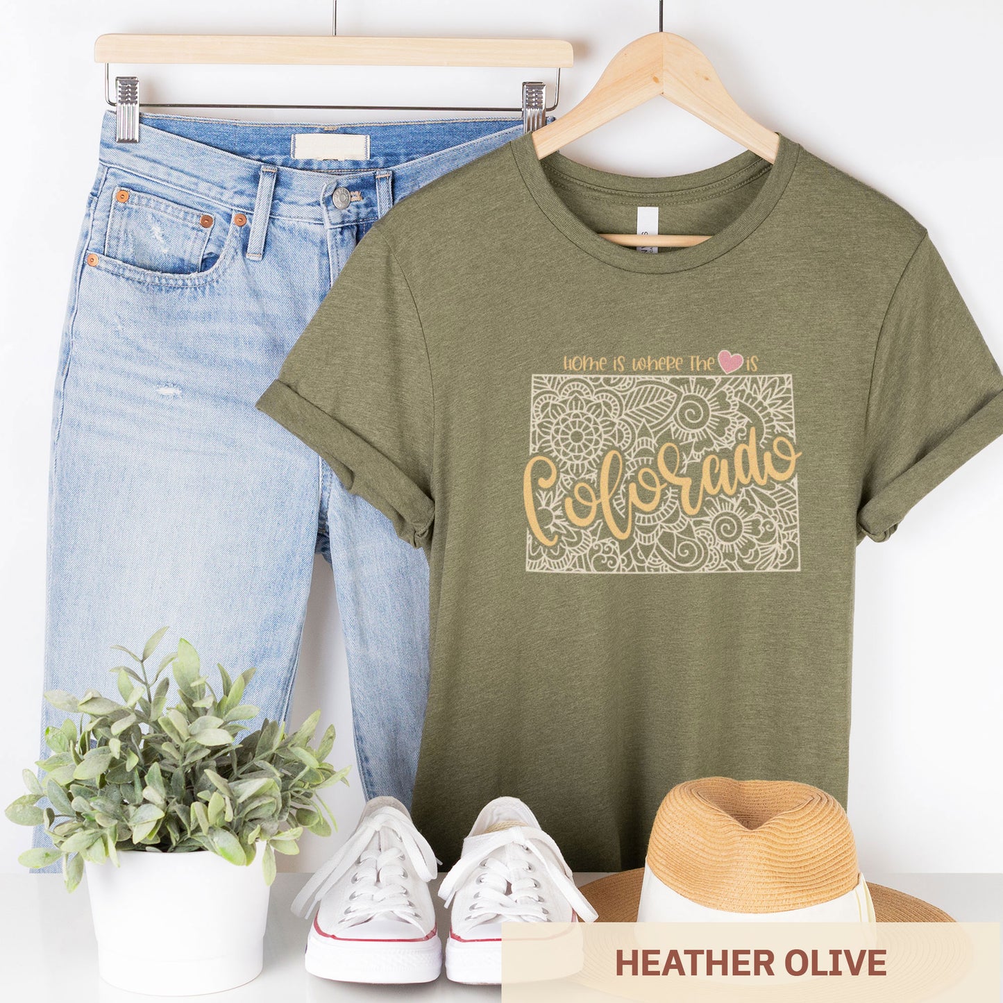 A hanging heather olive Bella Canvas t-shirt featuring a mandala in the shape of Colorado with the words home is where the heart is.