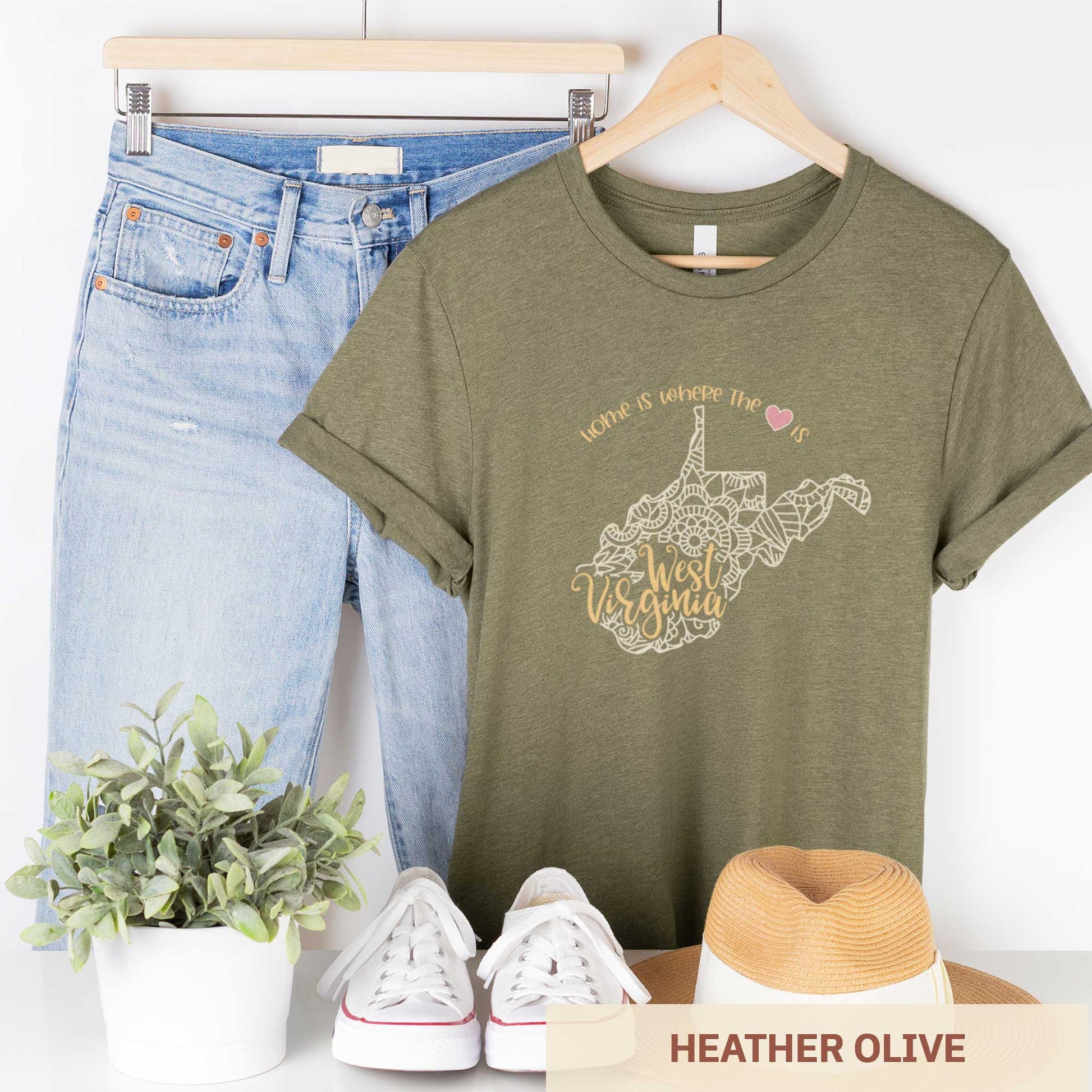 A hanging heather olive Bella Canvas t-shirt featuring a mandala in the shape of West Virginia with the words home is where the heart is.