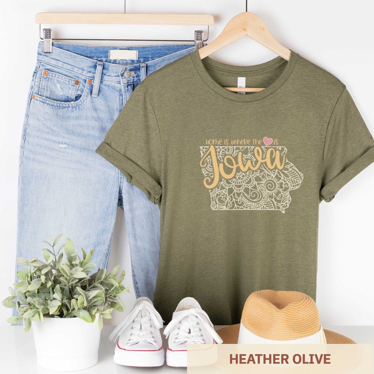 A hanging heather olive Bella Canvas t-shirt featuring a mandala in the shape of Iowa with the words home is where the heart is.