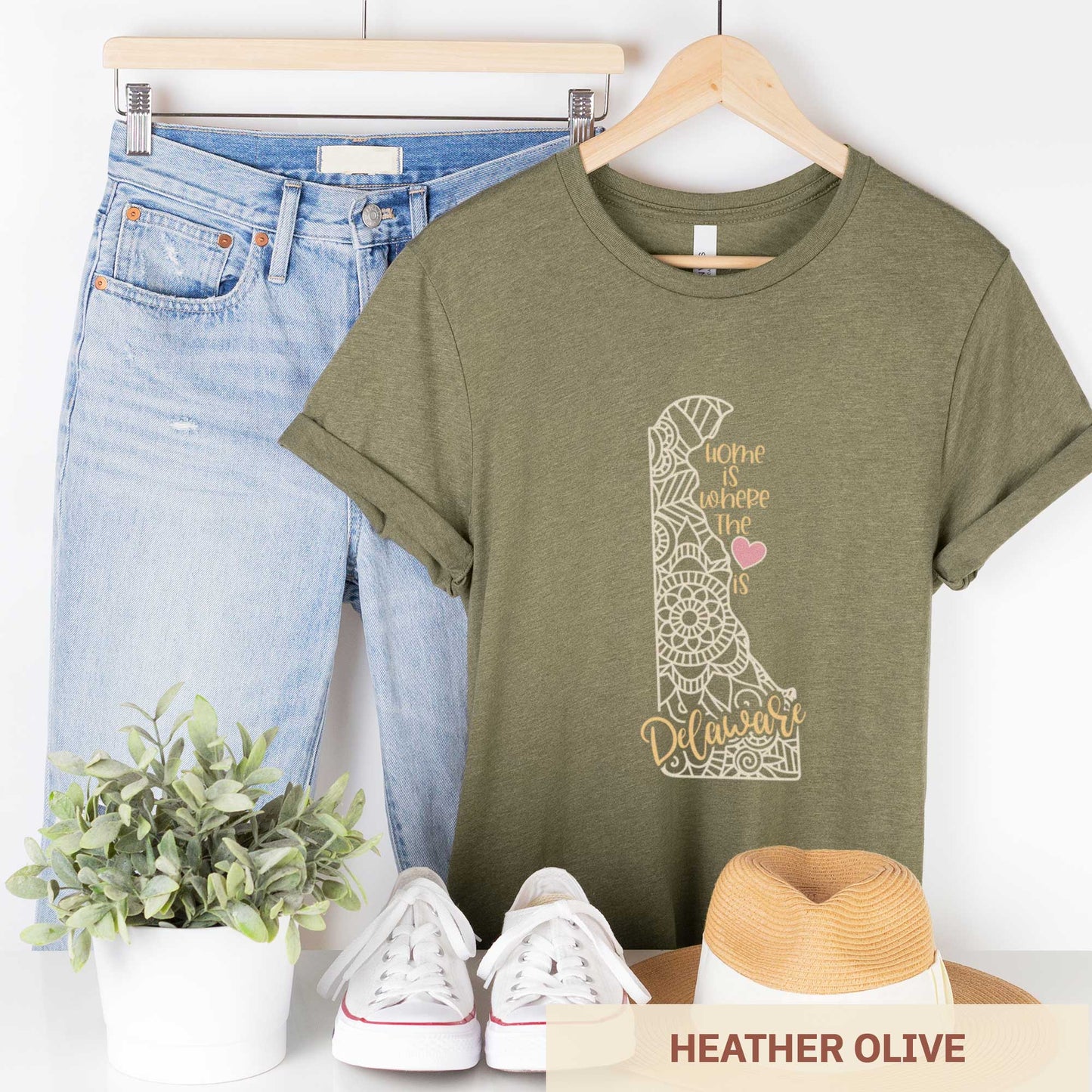 A hanging heather olive Bella Canvas t-shirt featuring a mandala in the shape of Delaware with the words home is where the heart is.