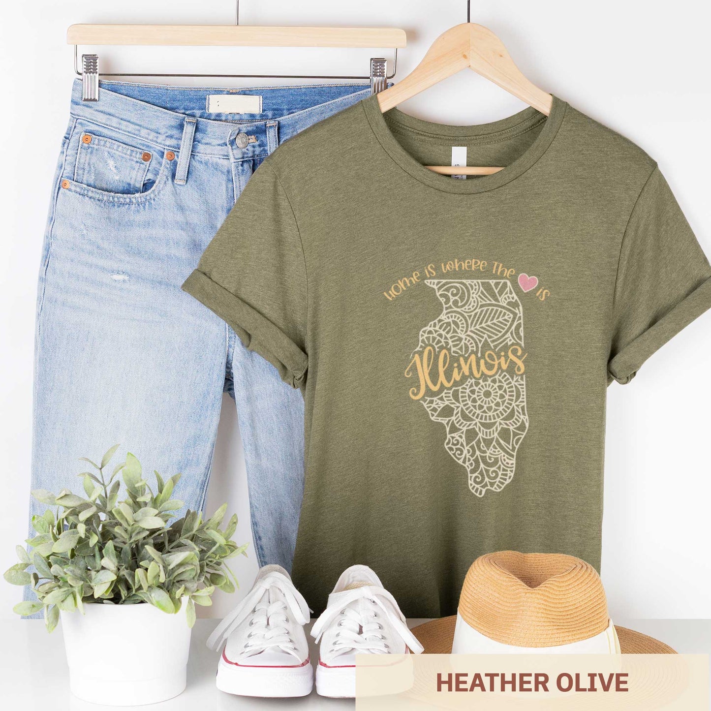 A hanging heather olive Bella Canvas t-shirt featuring a mandala in the shape of Illinois with the words home is where the heart is.