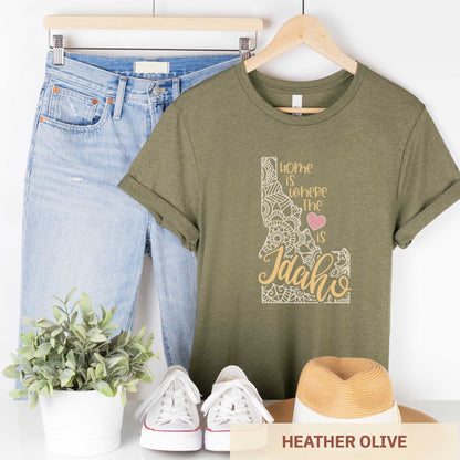 A hanging heather olive Bella Canvas t-shirt featuring a mandala in the shape of daho with the words home is where the heart is.