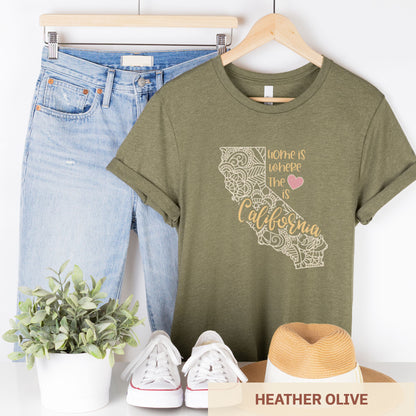 A hanging heather olive Bella Canvas t-shirt featuring a mandala in the shape of California with the words home is where the heart is.