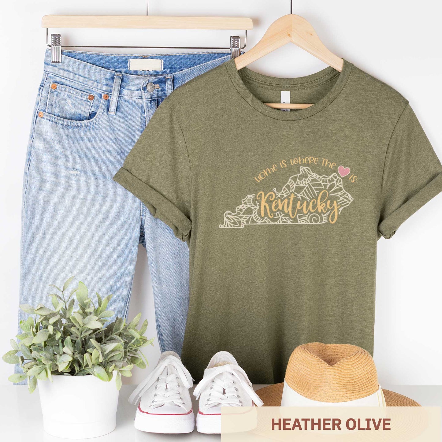 A hanging heather olive Bella Canvas t-shirt featuring a mandala in the shape of Kentucky with the words home is where the heart is.