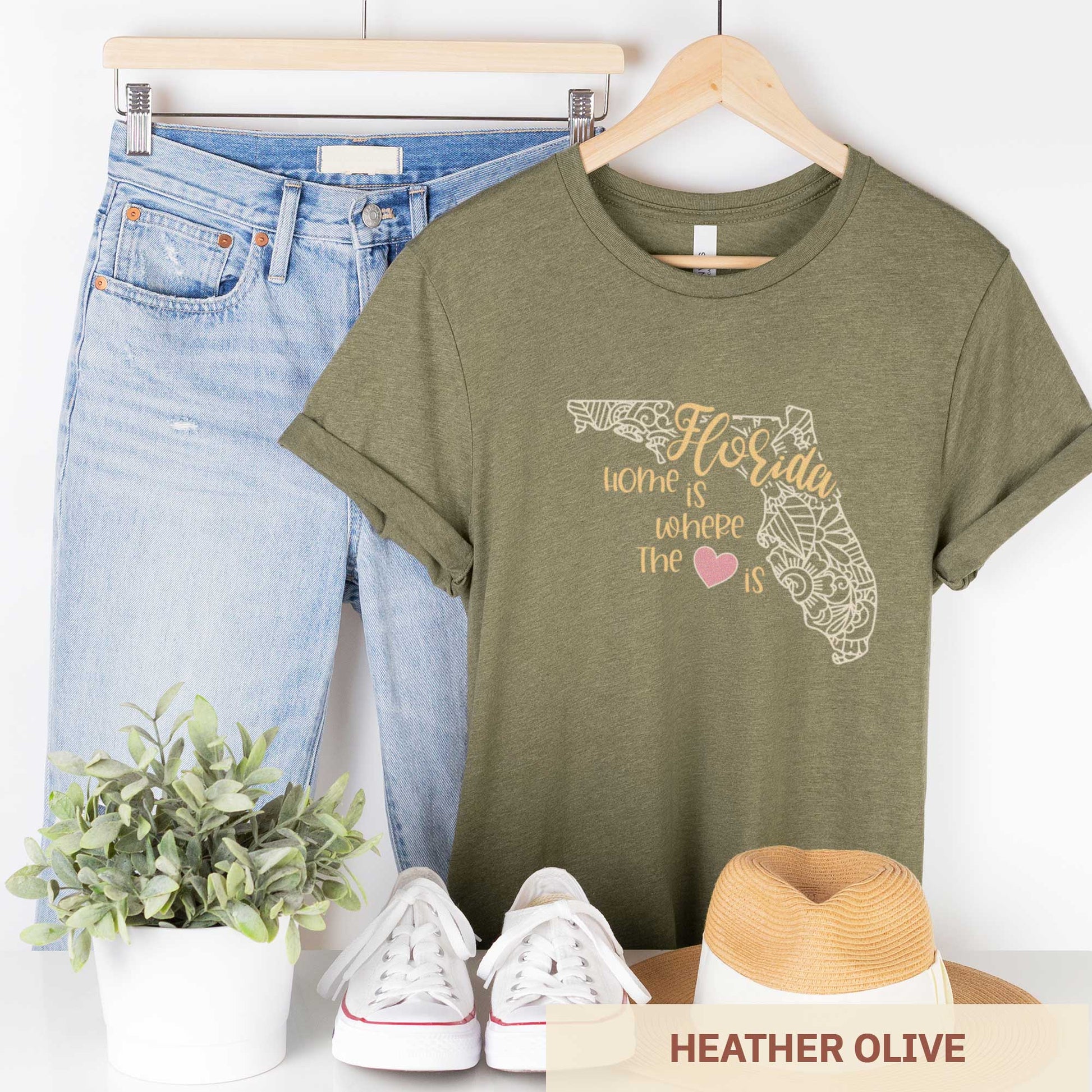 A hanging heather olive Bella Canvas t-shirt featuring a mandala in the shape of Florida with the words home is where the heart is.