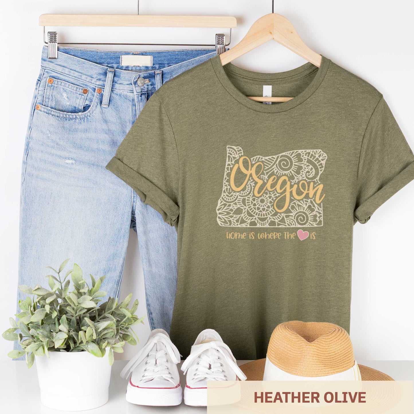 A hanging heather olive Bella Canvas t-shirt featuring a mandala in the shape of Oregon with the words home is where the heart is.
