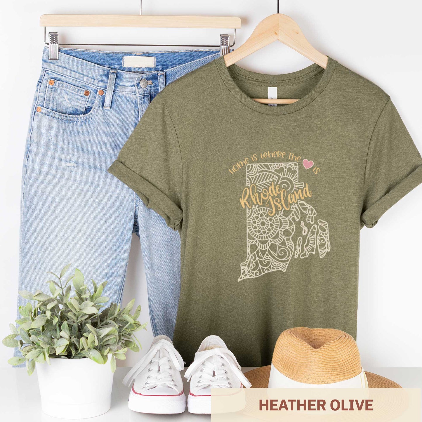 A hanging heather olive Bella Canvas t-shirt featuring a mandala in the shape of Rhode Island with the words home is where the heart is.