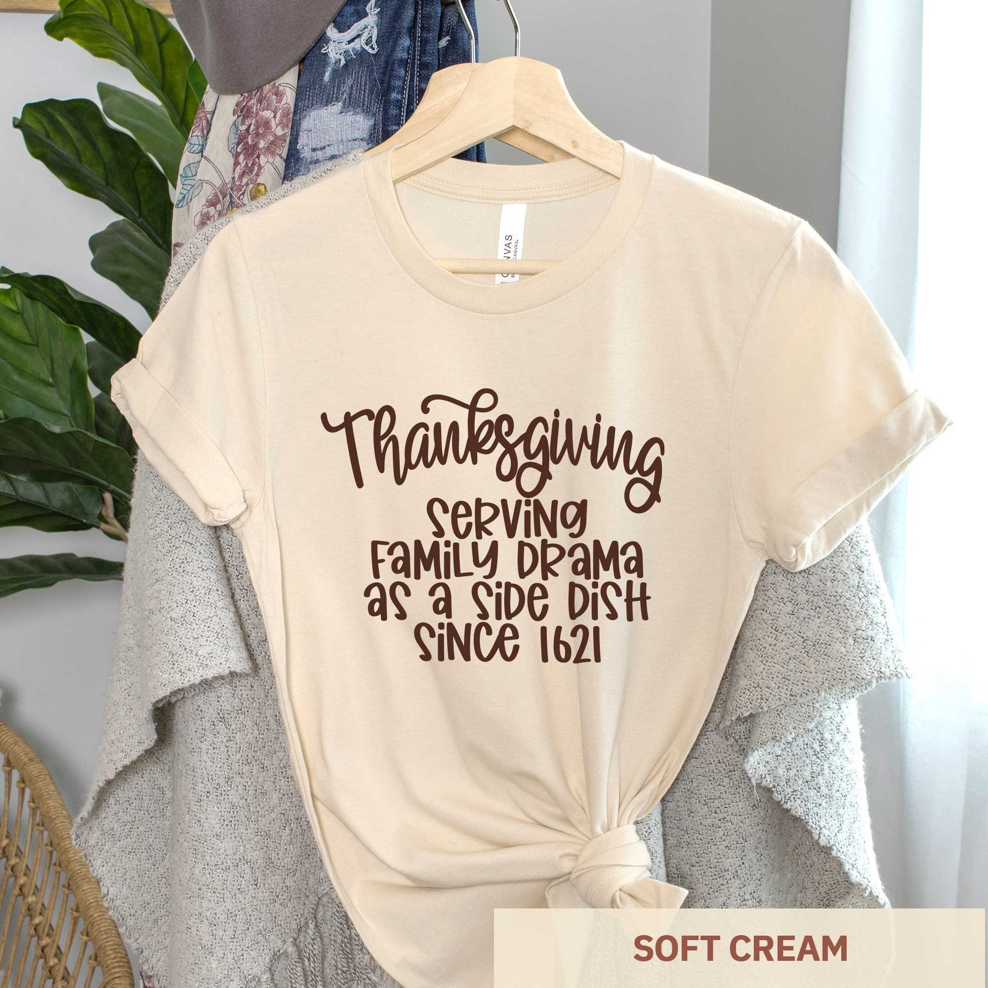 A hanging soft cream Bella Canvas t-shirt featuring the words thanksgiving serving family as a side dish since 1621.