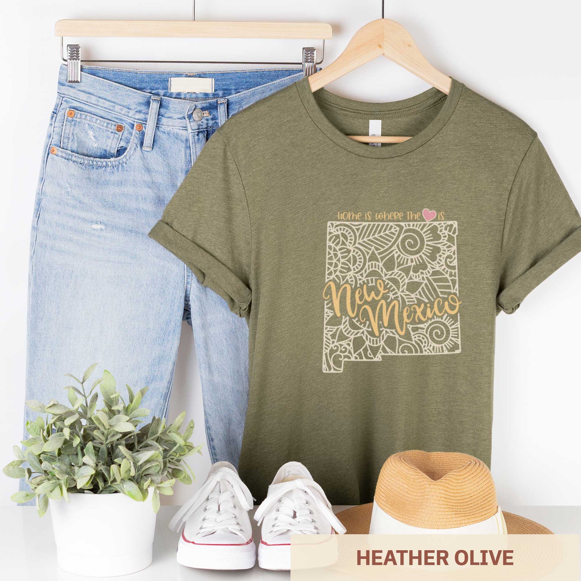 A hanging heather olive Bella Canvas t-shirt featuring a mandala in the shape of New Mexico with the words home is where the heart is.