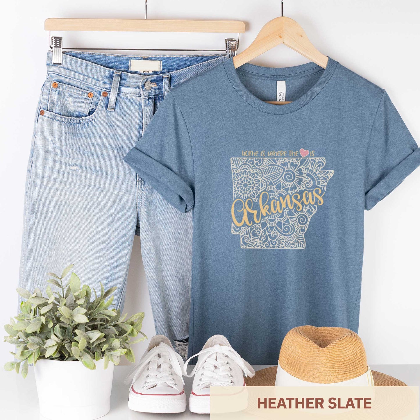 A hanging heather slate Bella Canvas t-shirt featuring a mandala in the shape of Arkansas with the words home is where the heart is.