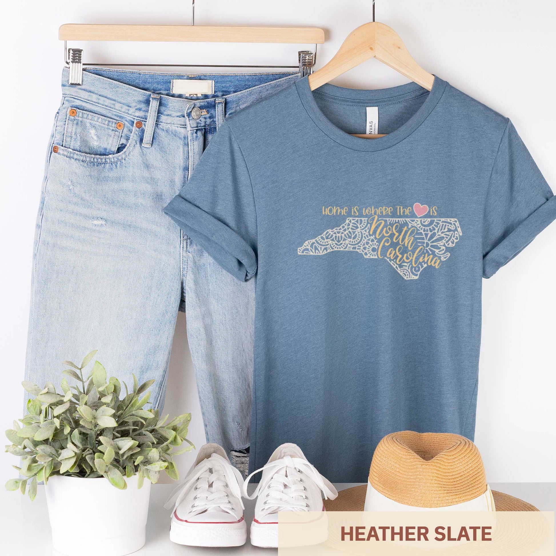 A hanging heather slate Bella Canvas t-shirt featuring a mandala in the shape of North Carolina with the words home is where the heart is.