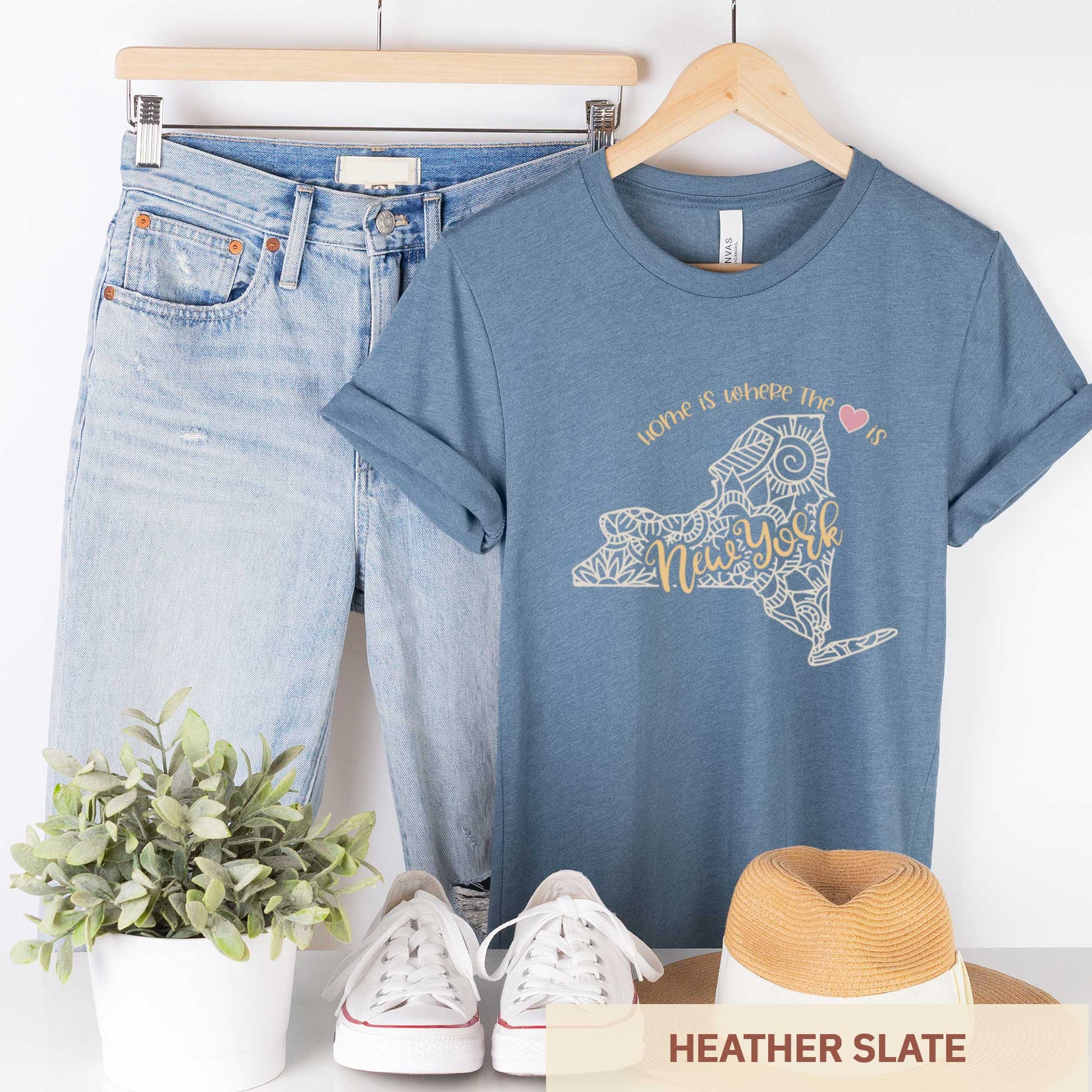 A hanging heather slate Bella Canvas t-shirt featuring a mandala in the shape of New York with the words home is where the heart is.