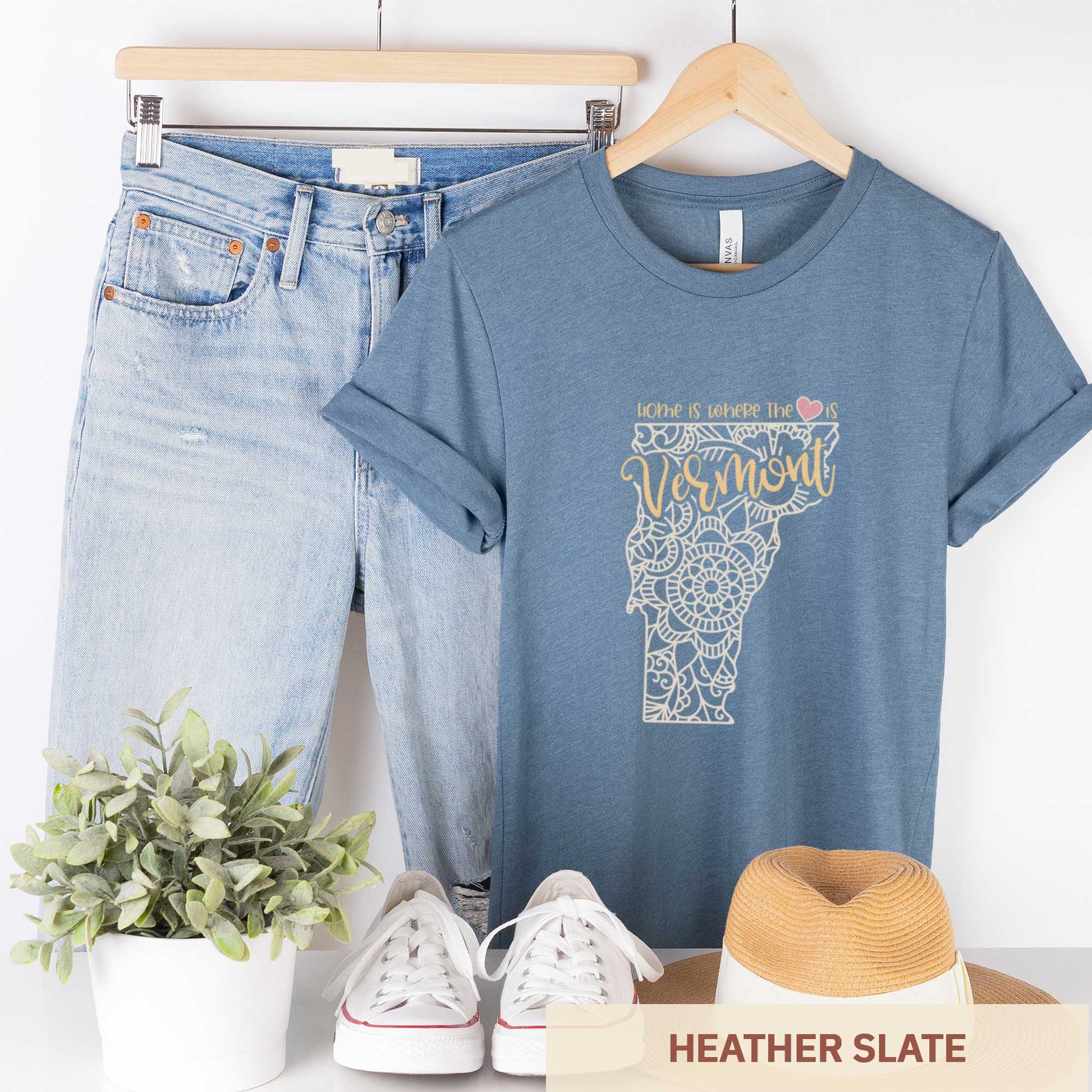A hanging heather slate Bella Canvas t-shirt featuring a mandala in the shape of Vermont with the words home is where the heart is.