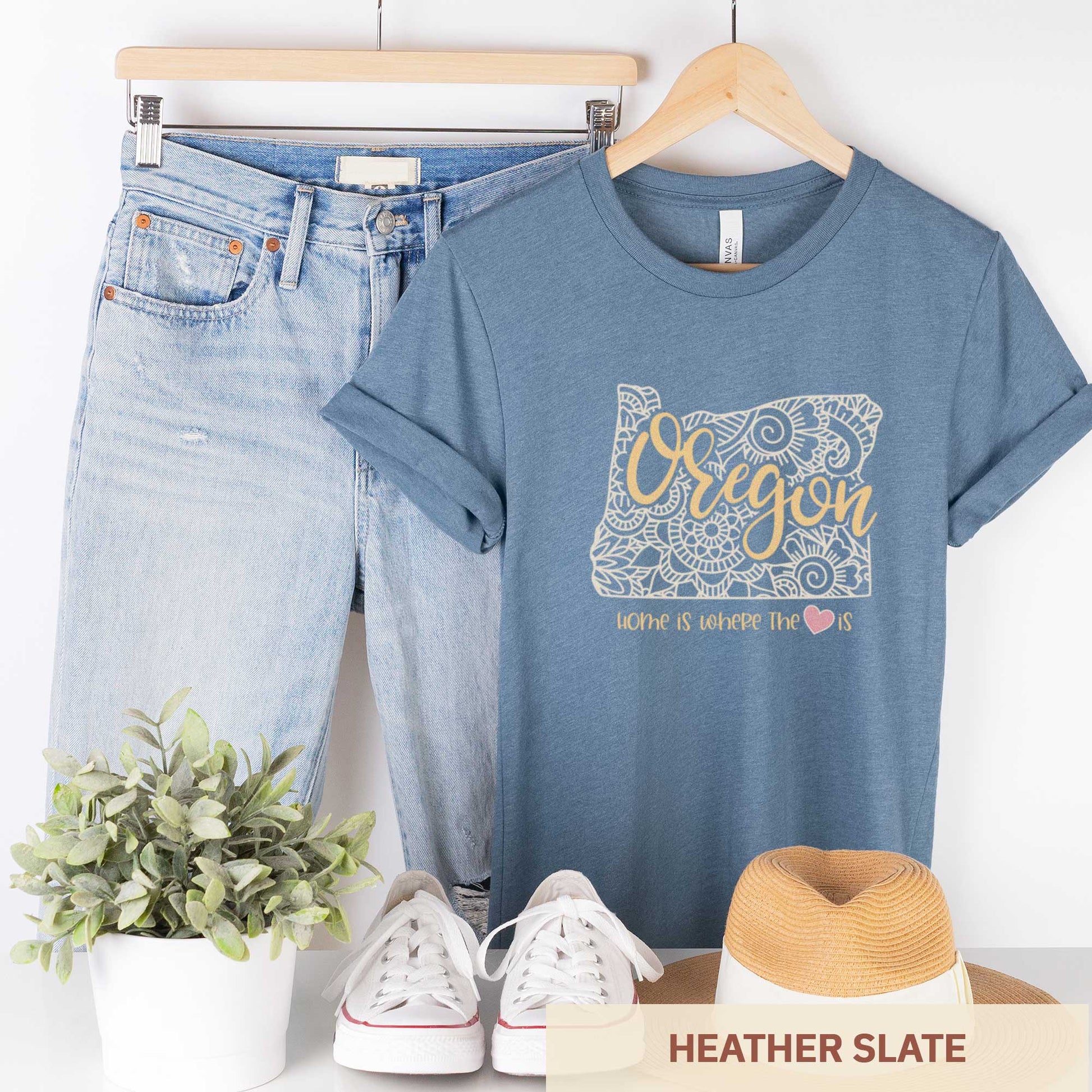 A hanging heather slate Bella Canvas t-shirt featuring a mandala in the shape of Oregon with the words home is where the heart is.