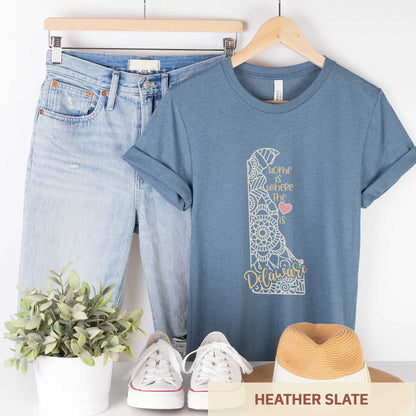 A hanging heather slate Bella Canvas t-shirt featuring a mandala in the shape of Delaware with the words home is where the heart is.
