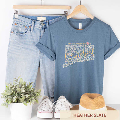 A hanging heather slate Bella Canvas t-shirt featuring a mandala in the shape of Connecticut with the words home is where the heart is.