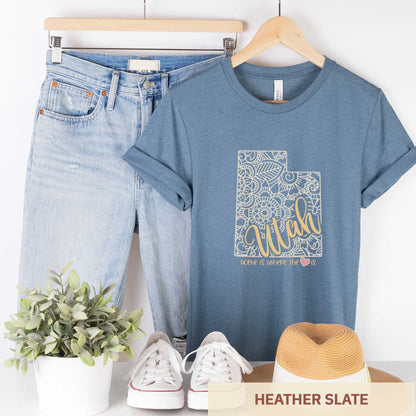 A hanging heather slate Bella Canvas t-shirt featuring a mandala in the shape of Utah with the words home is where the heart is.