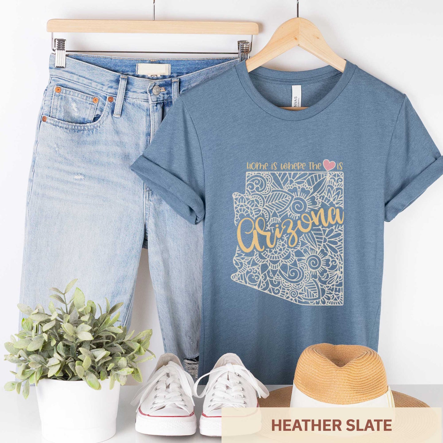 A hanging heather slate Bella Canvas t-shirt featuring a mandala in the shape of Arizona with the words home is where the heart is.