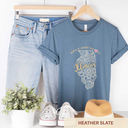 A hanging heather slate Bella Canvas t-shirt featuring a mandala in the shape of Illinois with the words home is where the heart is.