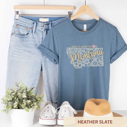 A hanging heather slate Bella Canvas t-shirt featuring a mandala in the shape of Montana with the words home is where the heart is.