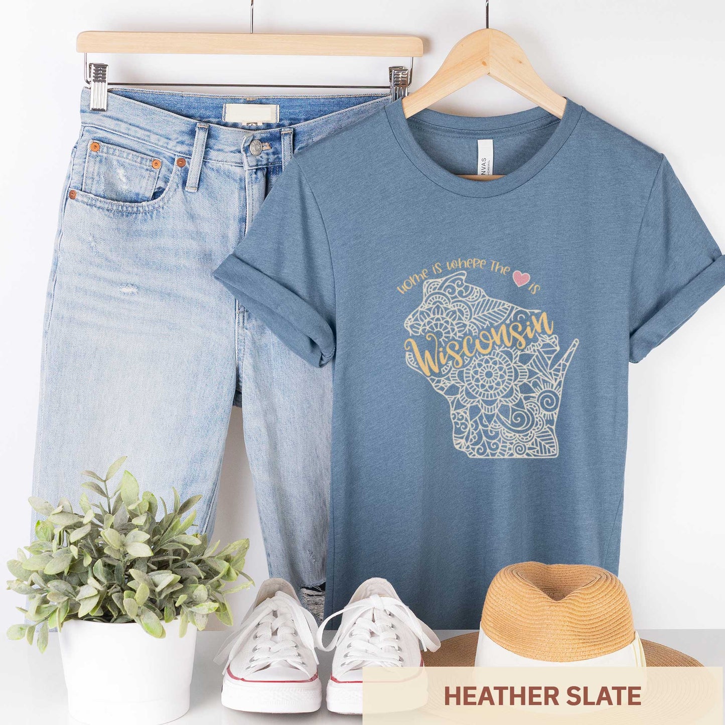 A hanging heather slate Bella Canvas t-shirt featuring a mandala in the shape of Wisconsin with the words home is where the heart is.