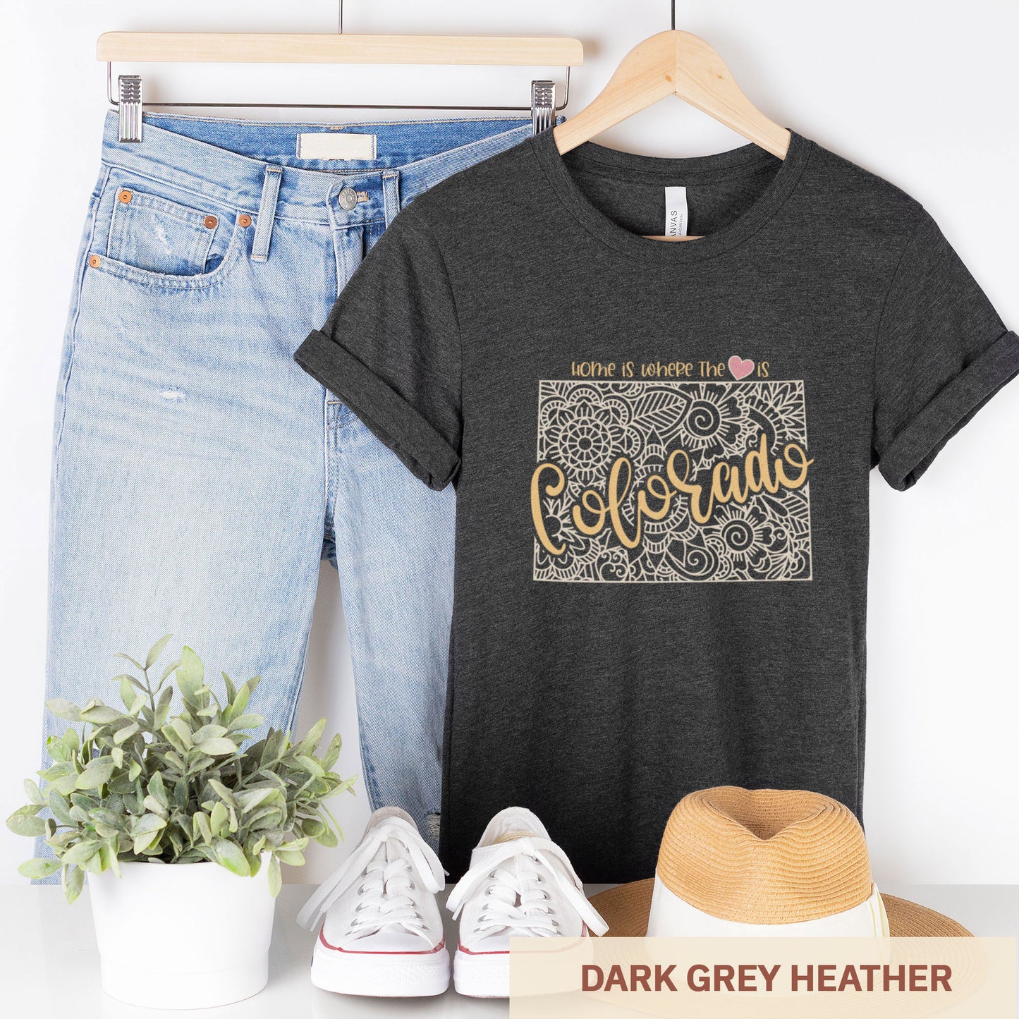  A hanging dark grey heather Bella Canvas t-shirt featuring a mandala in the shape of Colorado with the words home is where the heart is.