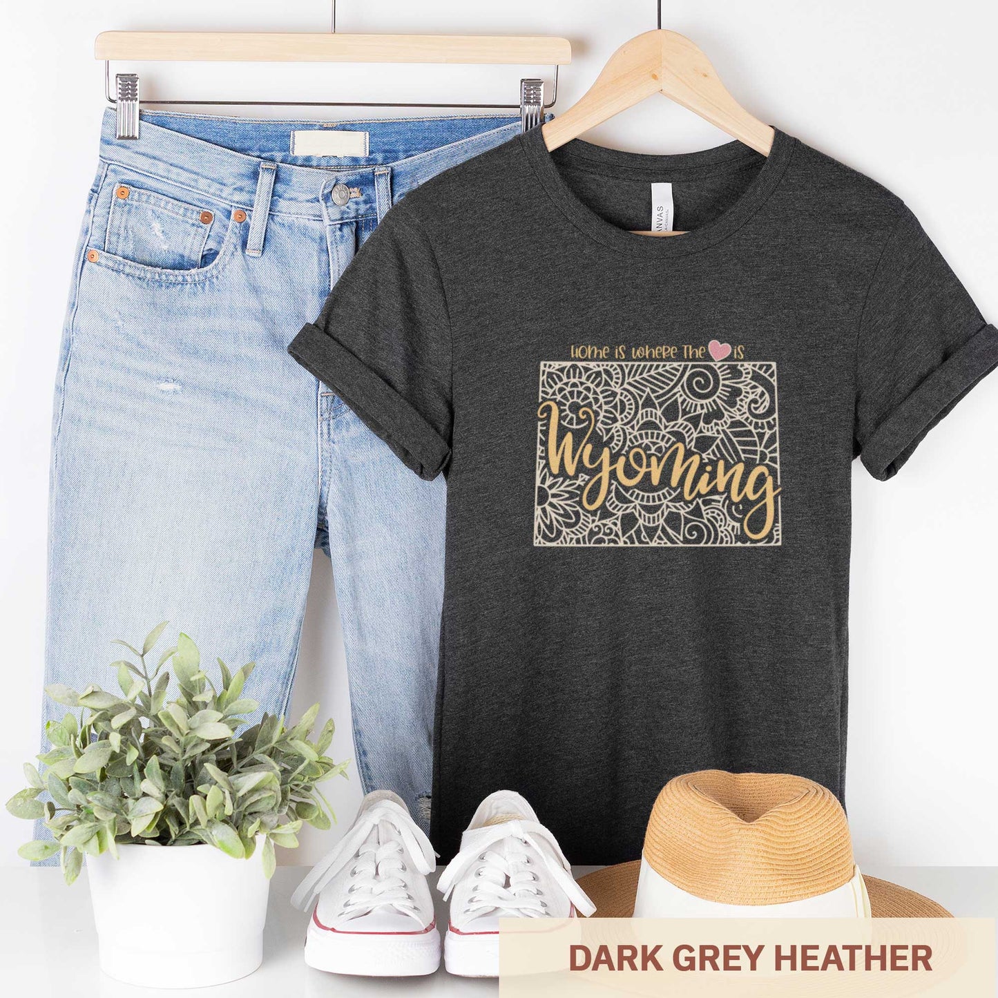 A hanging dark grey heather Bella Canvas t-shirt featuring a mandala in the shape of Wyoming with the words home is where the heart is.