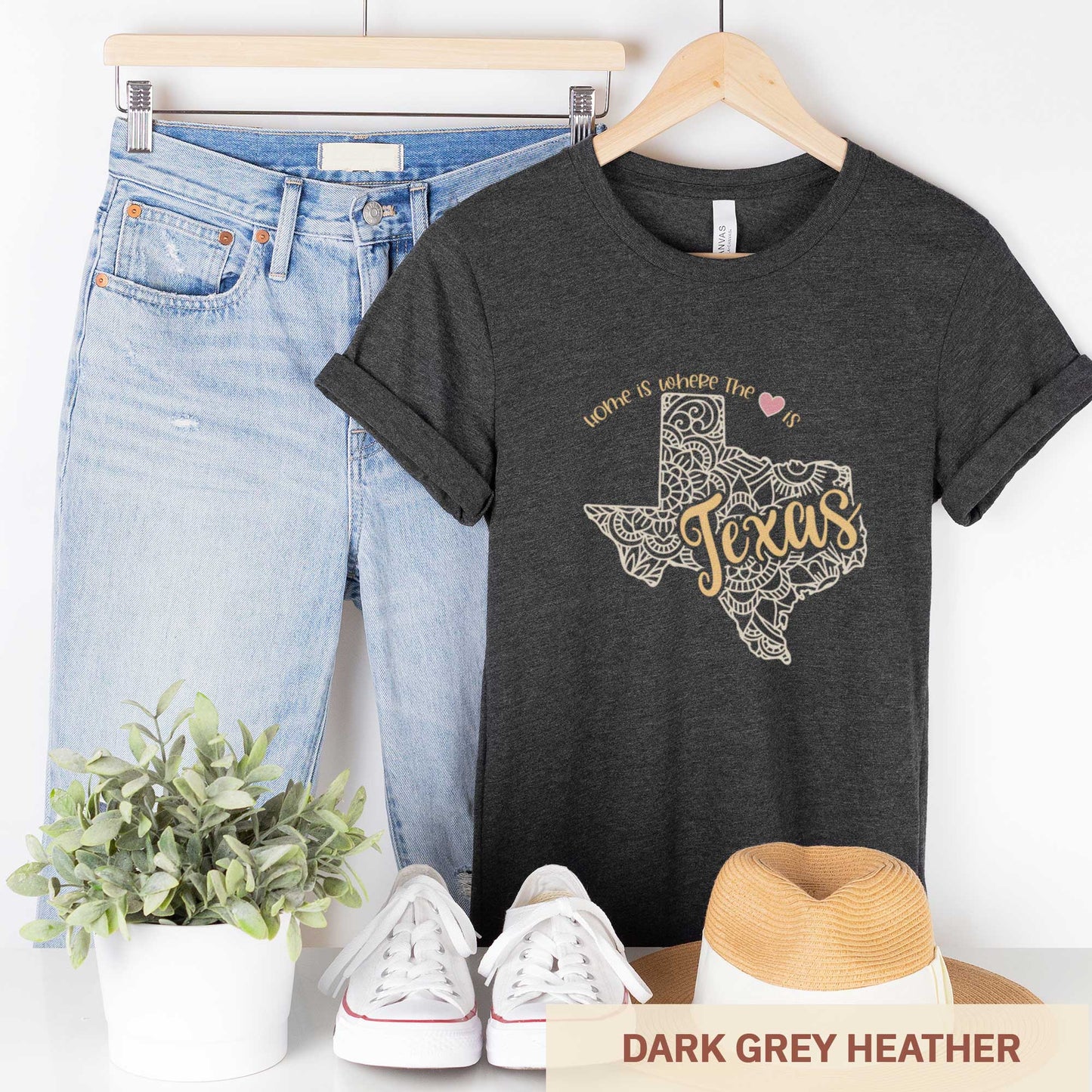 A hanging dark grey heather Bella Canvas t-shirt featuring a mandala in the shape of Texas with the words home is where the heart is.