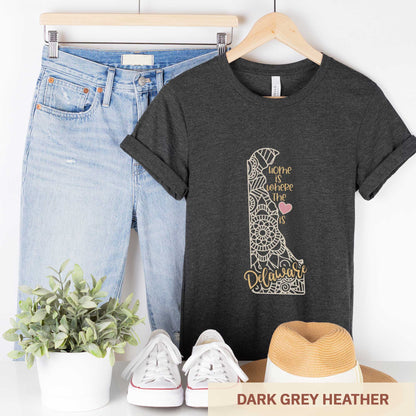 A hanging dark grey heather Bella Canvas t-shirt featuring a mandala in the shape of Delaware with the words home is where the heart is.