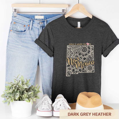 A hanging dark grey heather Bella Canvas t-shirt featuring a mandala in the shape of New Mexico with the words home is where the heart is.