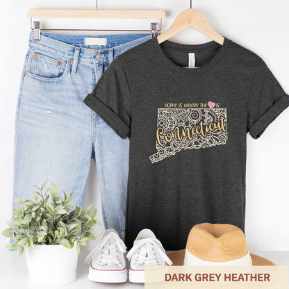 A hanging dark grey heather Bella Canvas t-shirt featuring a mandala in the shape of Connecticut with the words home is where the heart is.