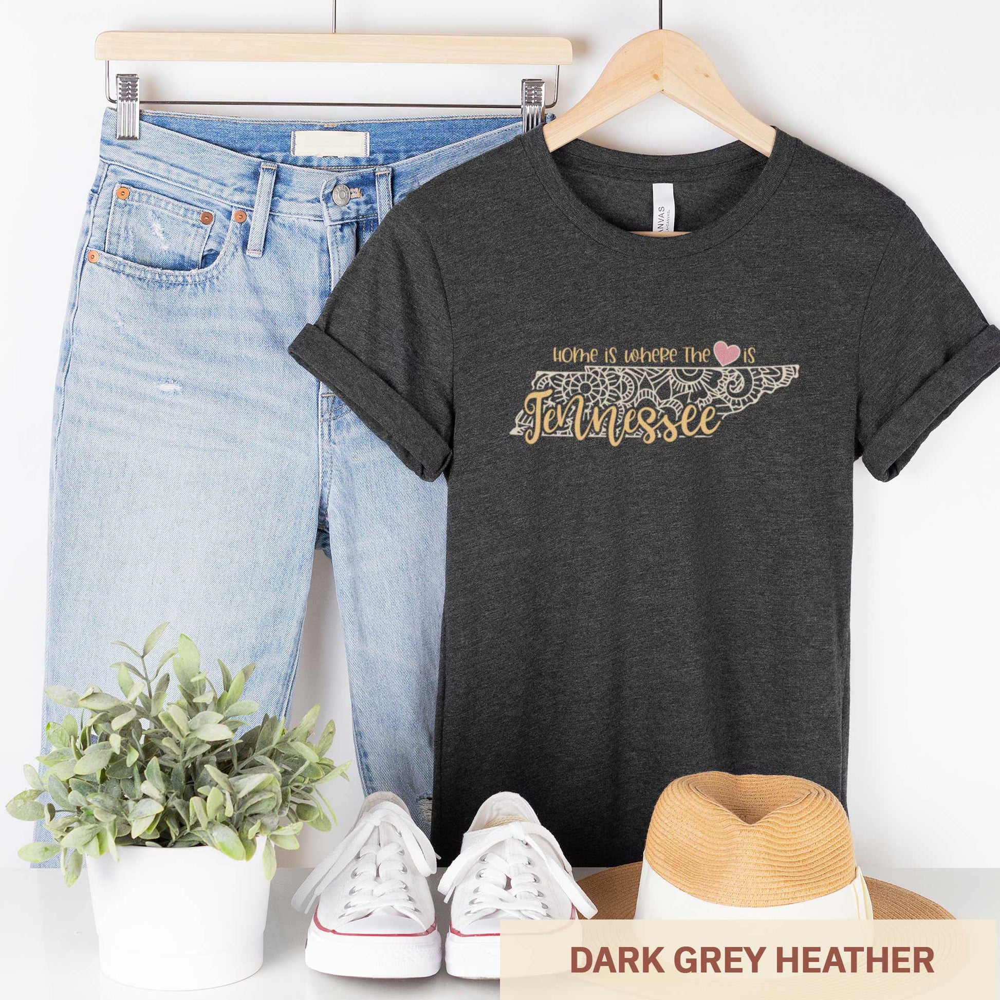 A hanging dark grey heather Bella Canvas t-shirt featuring a mandala in the shape of Tennessee with the words home is where the heart is.
