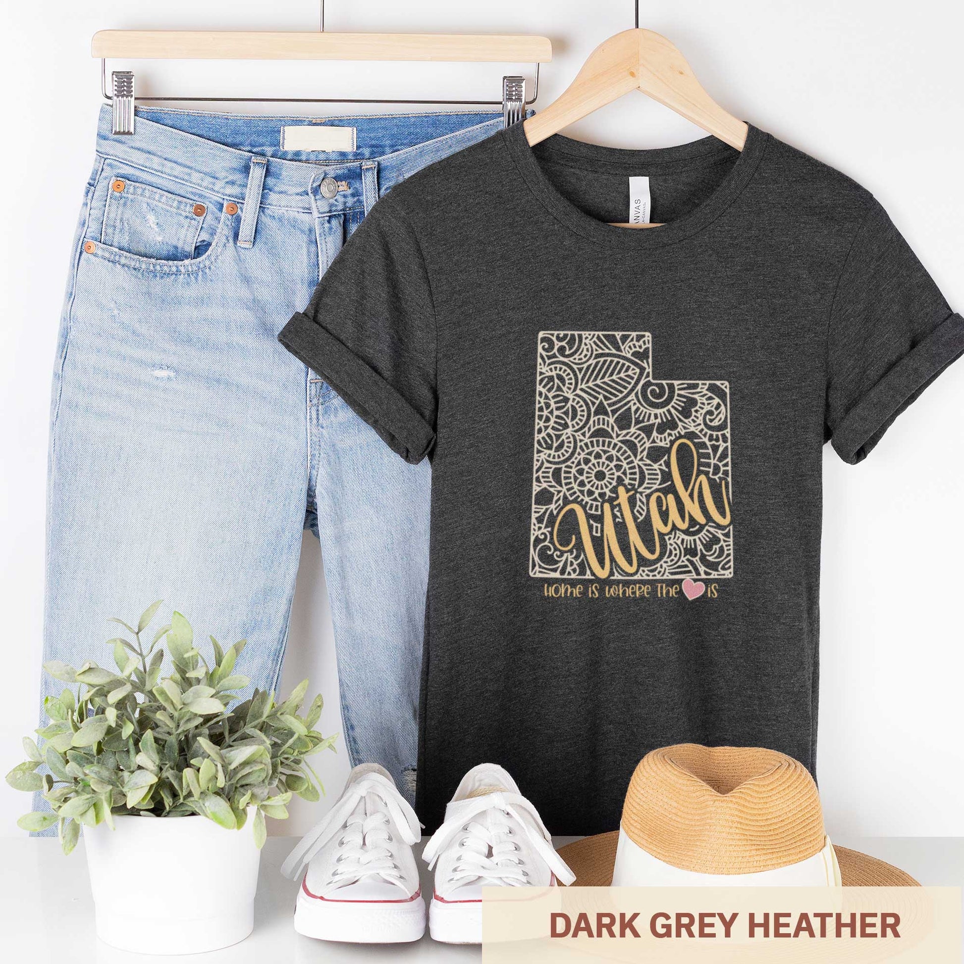 A hanging dark grey heather Bella Canvas t-shirt featuring a mandala in the shape of Utah with the words home is where the heart is.