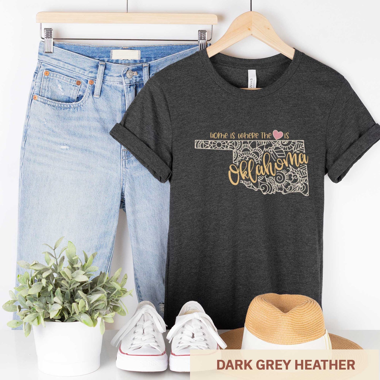 A hanging dark grey heather Bella Canvas t-shirt featuring a mandala in the shape of Oklahoma with the words home is where the heart is.