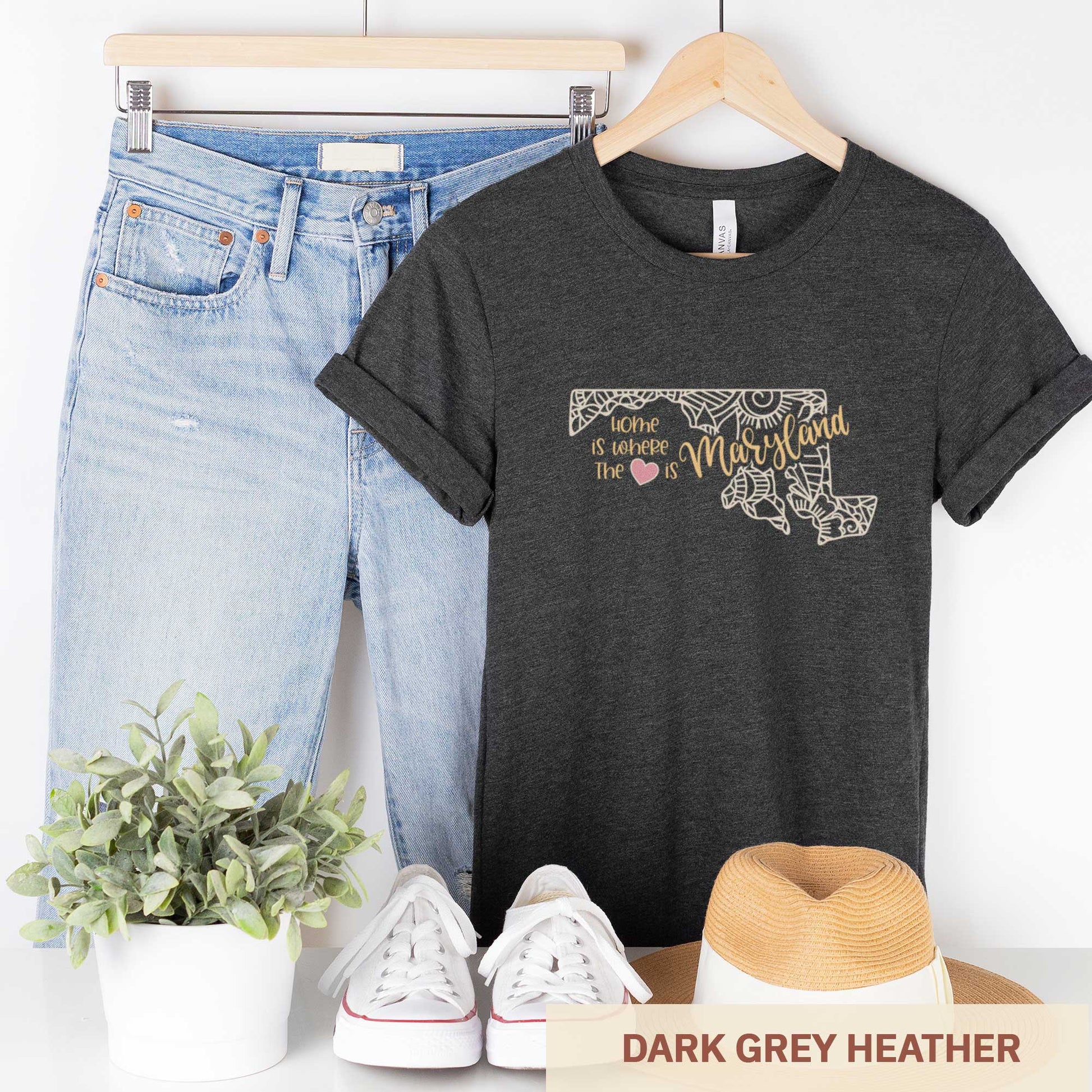 A hanging dark grey heather Bella Canvas t-shirt featuring a mandala in the shape of Maryland with the words home is where the heart is.