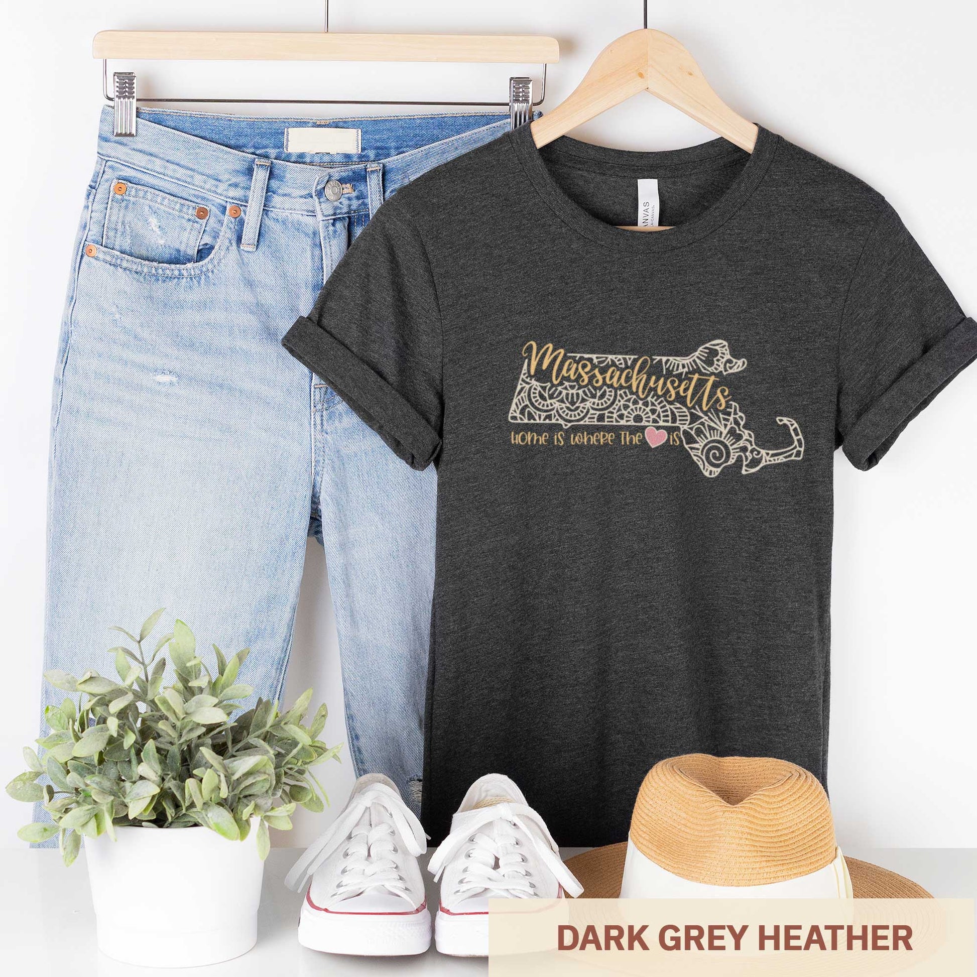 A hanging dark grey heather Bella Canvas t-shirt featuring a mandala in the shape of Massachusetts with the words home is where the heart is.