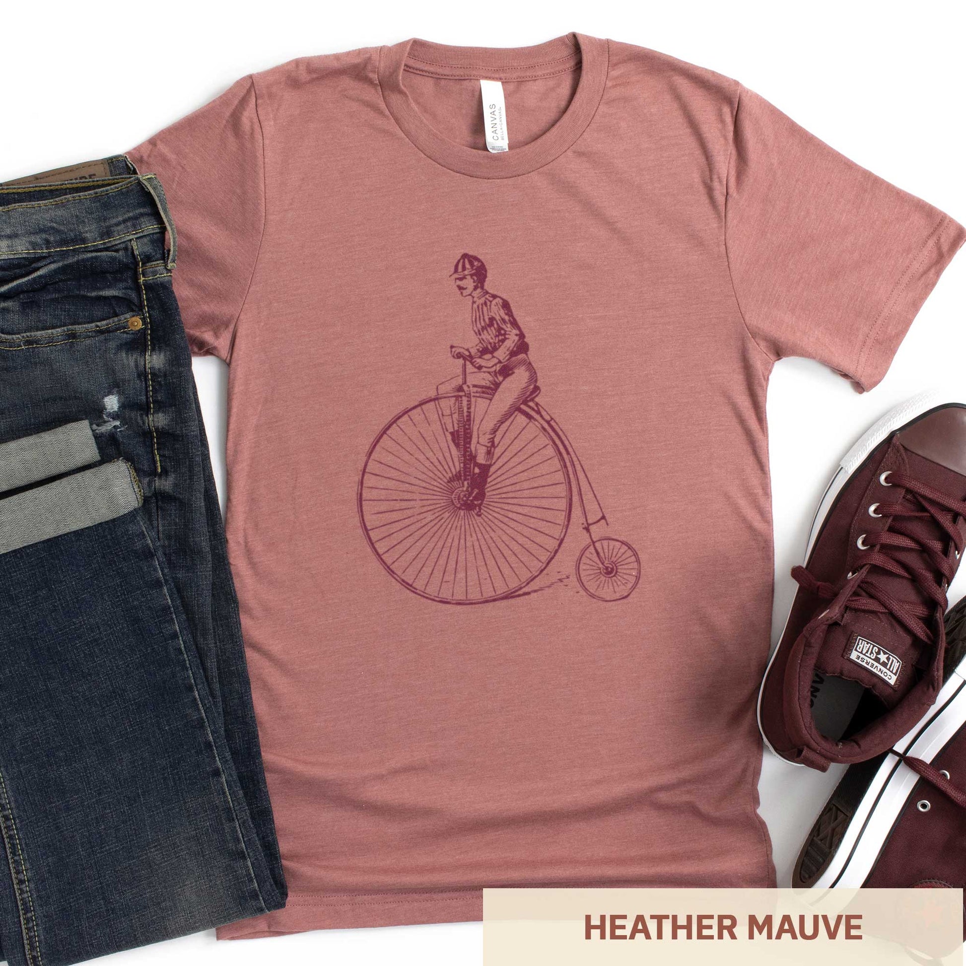 An heather mauve Bella Canvas t-shirt featuring a Victorian man riding a penny farthing bicycle.