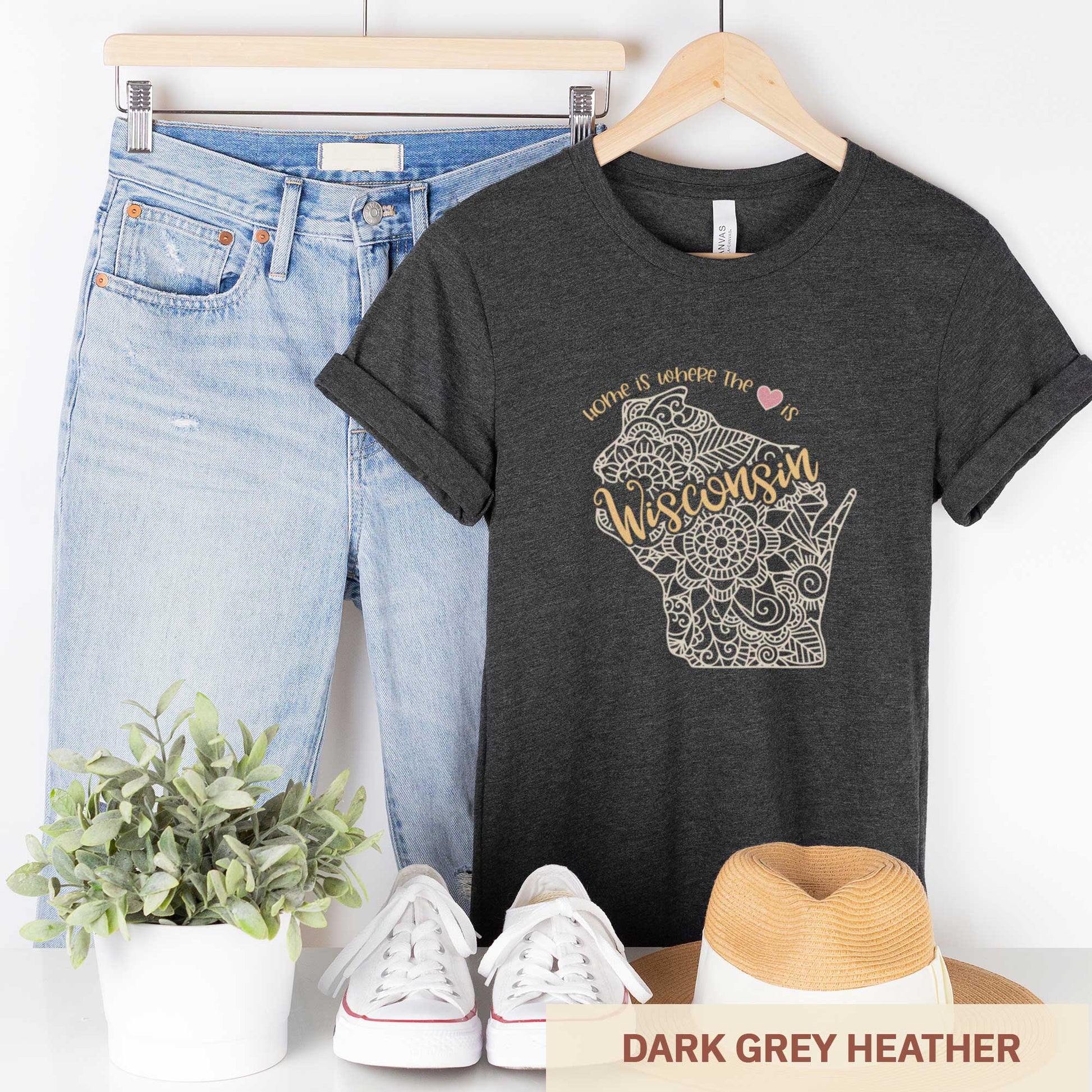 A hanging dark grey heather Bella Canvas t-shirt featuring a mandala in the shape of Wisconsin with the words home is where the heart is.