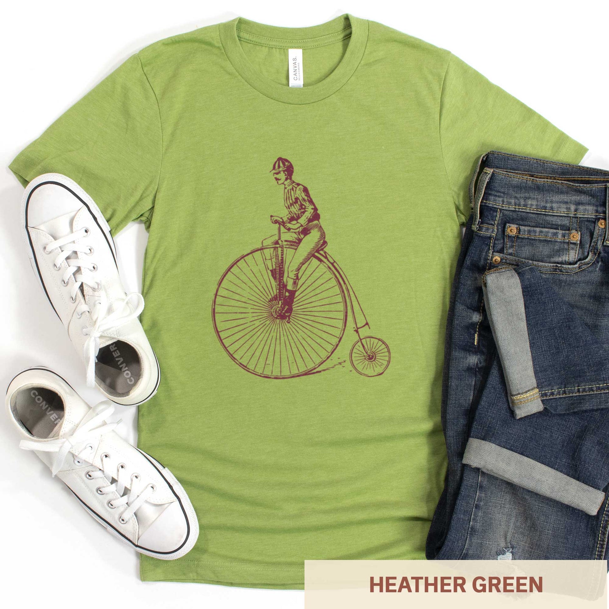 An heather green Bella Canvas t-shirt featuring a Victorian man riding a penny farthing bicycle.
