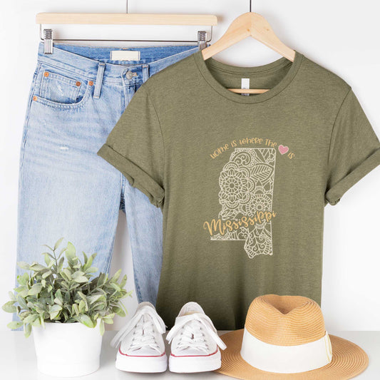 A hanging heather olive Bella Canvas t-shirt featuring a mandala in the shape of Mississippi with the words home is where the heart is.