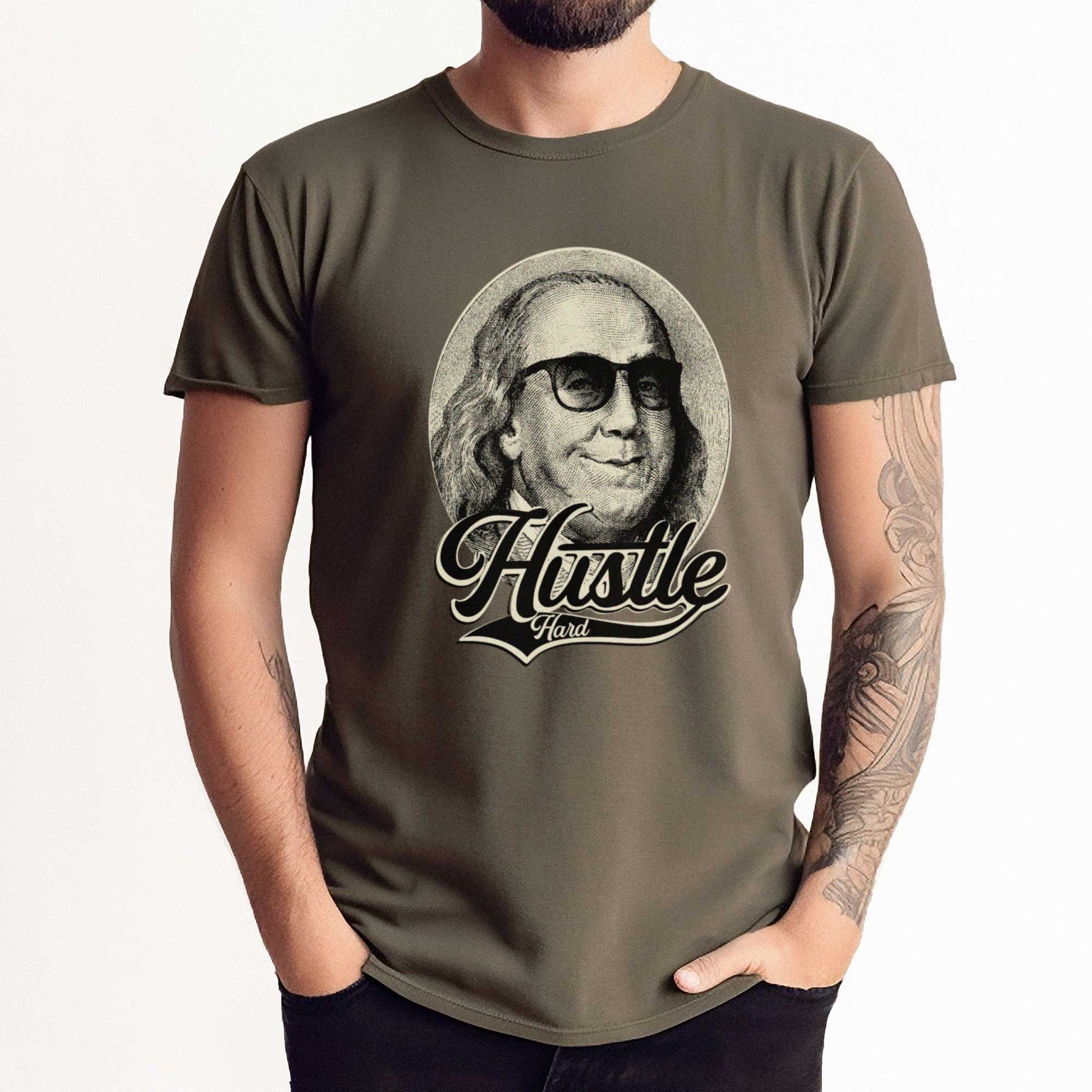 A man wearing an army green Bella Canvas t-shirt that features Benjamin Franklin in sunglasses with the words hustle hard.