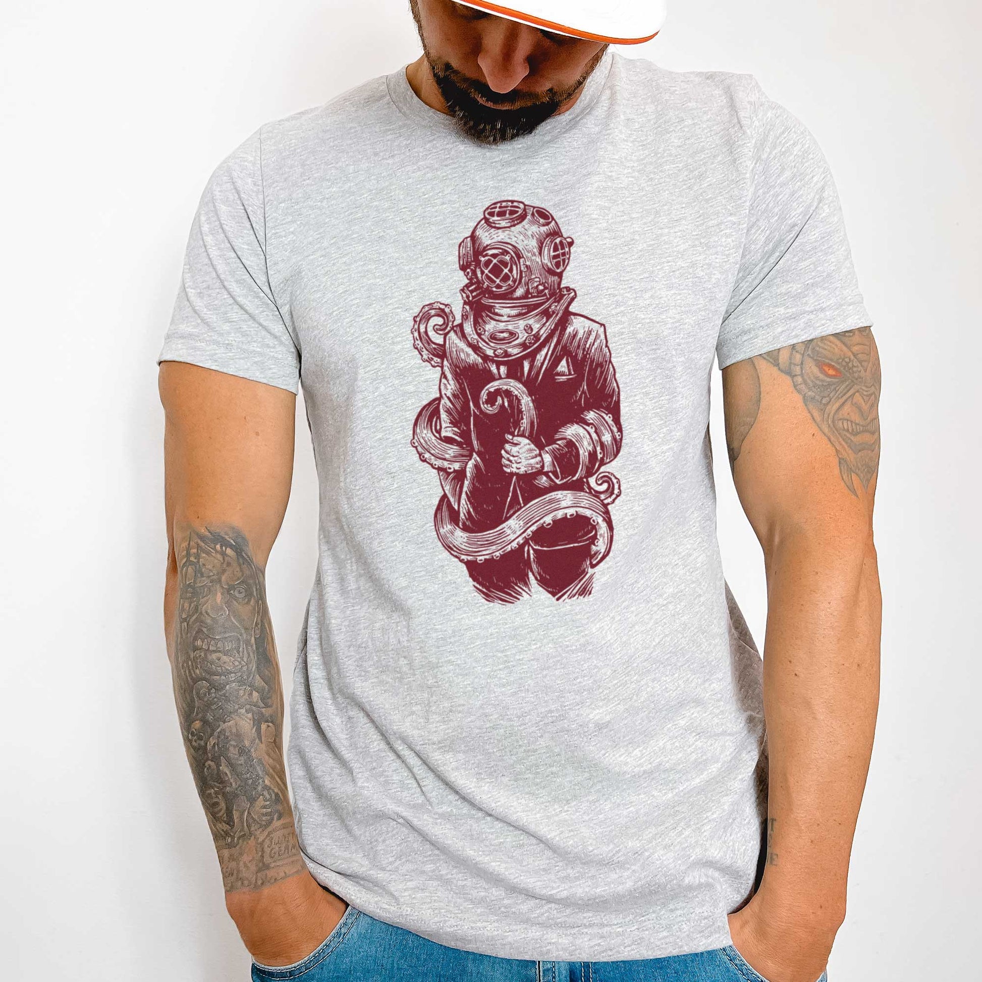 A man wearing an athletic heather Bella Canvas t-shirt featuring a figure in a business suit wearing a vintage diver's helmet with octopus tentacles wrapped around them.