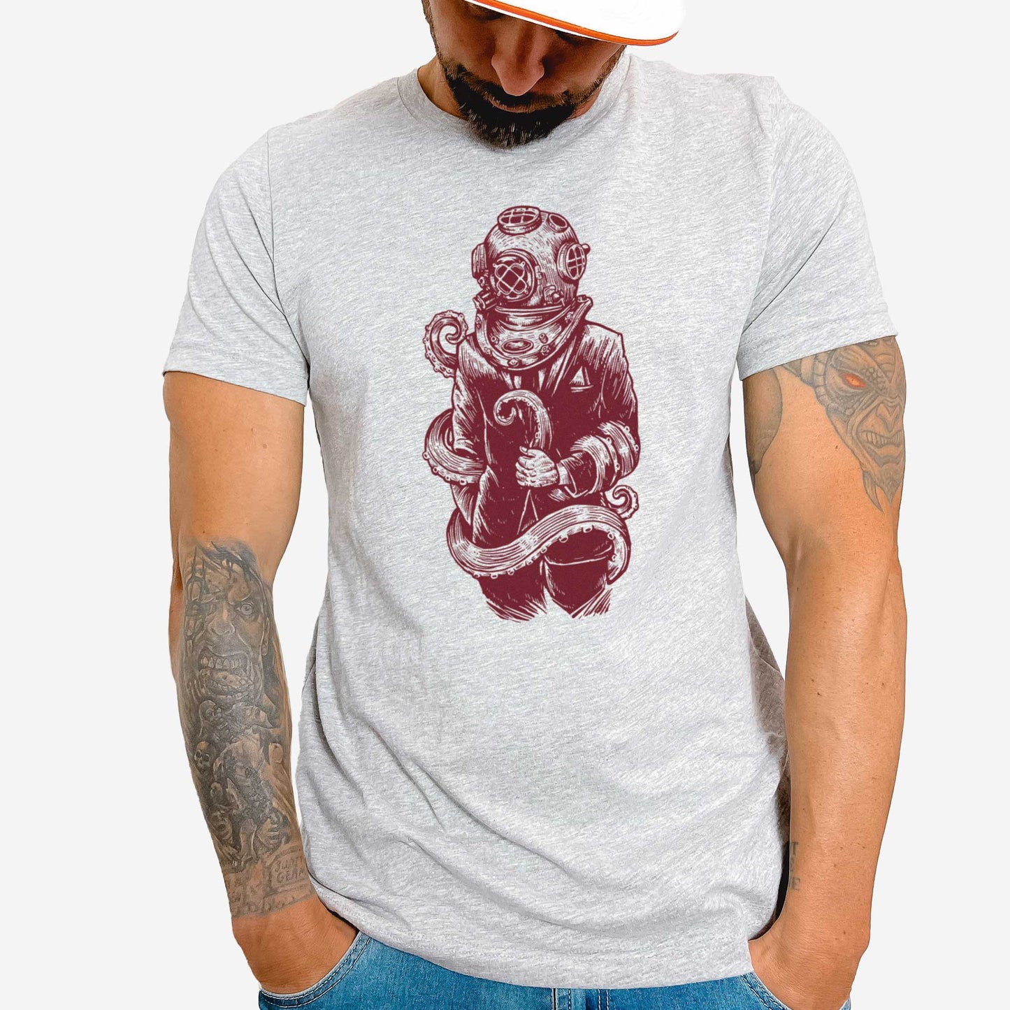 A man wearing an athletic heather Bella Canvas t-shirt featuring a figure in a business suit wearing a vintage diver's helmet with octopus tentacles wrapped around them.
